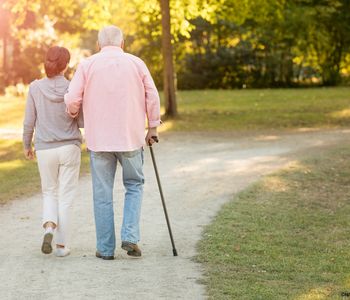 Symbolbild: Frau geht mit älterem Mann am Stock im Park spazieren