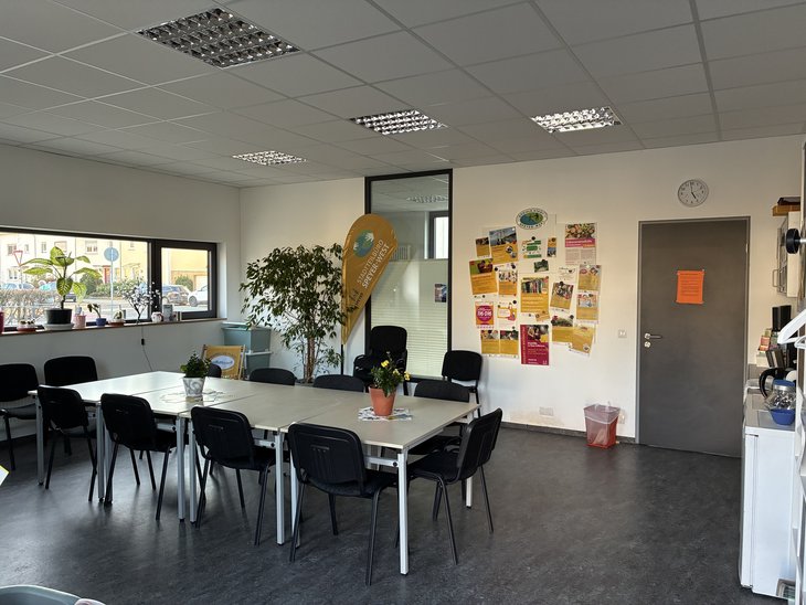 Ein Blick in das Stadtteilbüro Speyer-West: Das Foto zeigt einen großen Tisch mit Stühlen und eine Beachflag mit der Aufschrift "Stadtteilbüro"