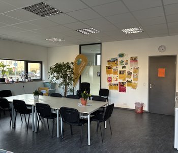 Ein Blick in das Stadtteilbüro Speyer-West: Das Foto zeigt einen großen Tisch mit Stühlen und eine Beachflag mit der Aufschrift "Stadtteilbüro".