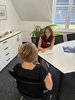 Lara Heß, eine junge Frau mit langen dunklen Haaren, sitzt mit einem Notizbuch am Tisch und berät eine Klientin, die vor ihr sitzt.