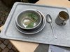 Ein Tablett mit einem Suppenteller und einer Tasse. Die Suppe besteht nur aus Wasser und ein paar Gemüseresten. Am Rand liegt eine kleine Scheibe Brot.