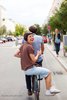 Symbolbild: Ein Fahrrad fährt auf der Straße, eine Frau sitzt auf dem Gepäckträger und winkt lachend in die Kamera