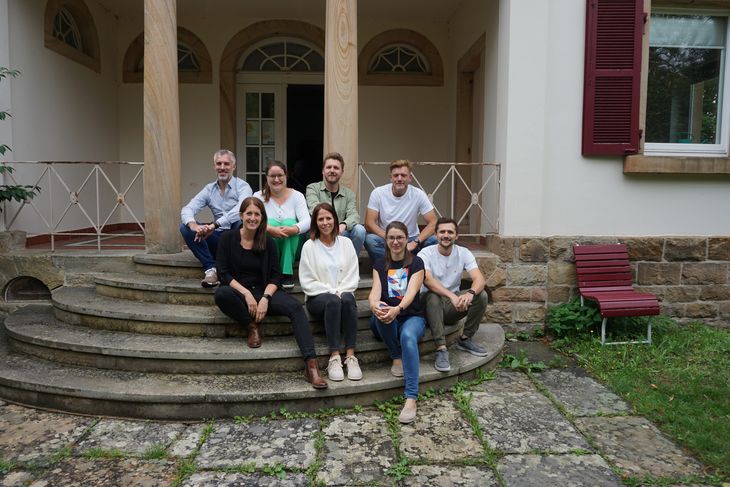 Auf dem Foto sind die aktuellen Trainees zu sehen, sie sitzen auf einer Treppe, arbeiten alle für das Pfalzklinikum.