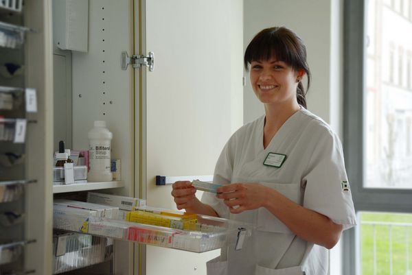 Eine in die Kamera lächelnde Pflegerin nimmt ein medizinisches Produkt aus einem Schrank