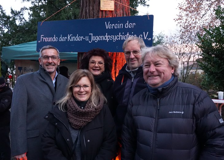 Der Vorstand des Fördervereins im Gruppenbild, dahinter ein blaues Schild mit der Aufschrift: "Verein der Freunde der Kinder- und Jugendpsychiatrie e.V."