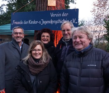 Der Vorstand des Fördervereins im Gruppenbild, dahinter ein blaues Schild mit der Aufschrift: "Verein der Freunde der Kinder- und Jugendpsychiatrie e.V."