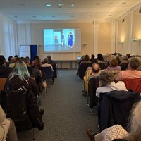 Das Bild zeigt den Konferenzraum mit dem Publikum und die Leinwand mit dem Video des Theaterstücks.