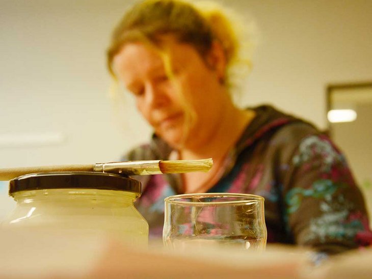 Im Vordergrund des Bildes sieht man einen Malpinsel und im Hintergrund ist eine Frau abgebildet