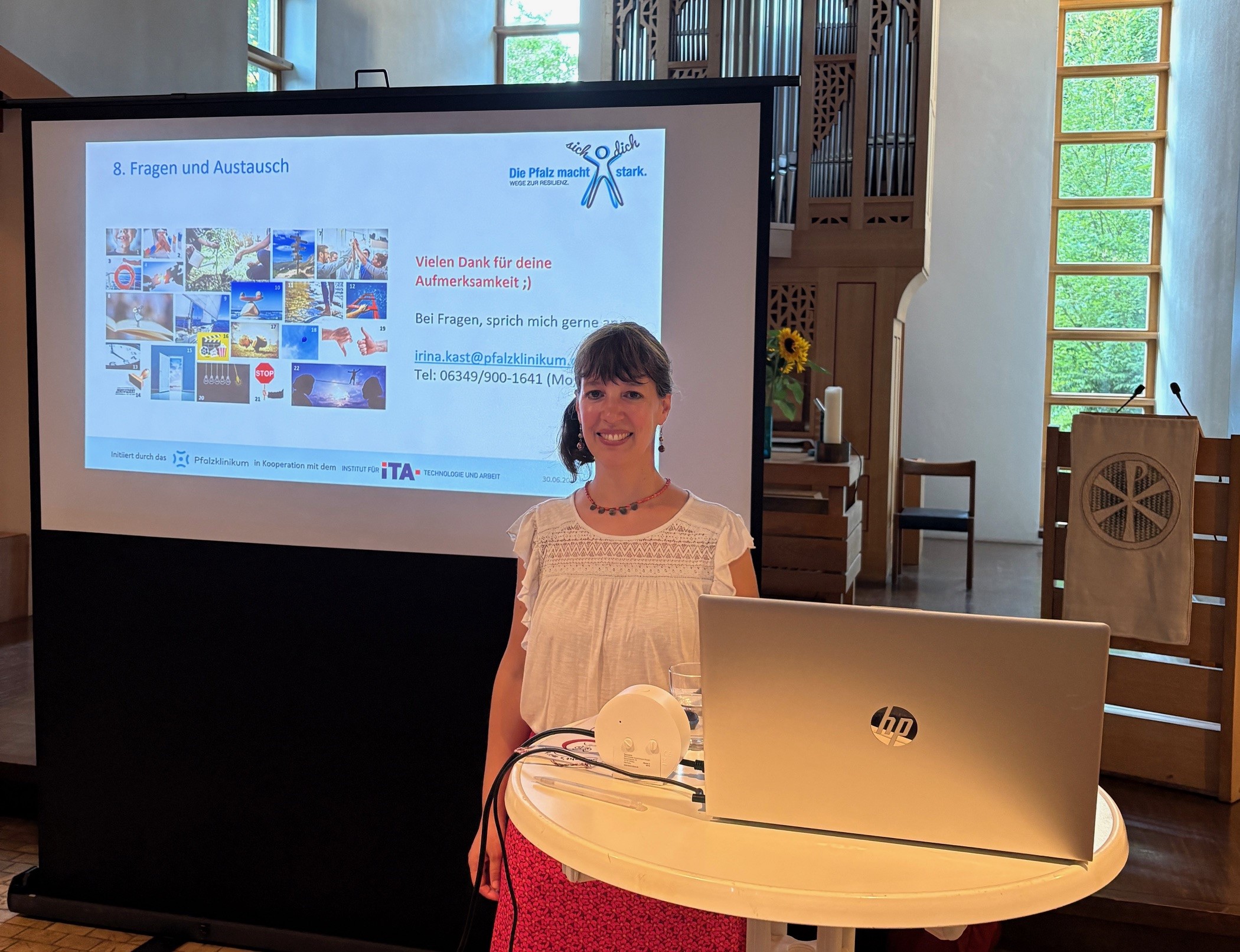 Irina Kast bei einem Vortrag mit Laptop im Vordergrund und einer Powerpointpräsentation im Hintergrund.